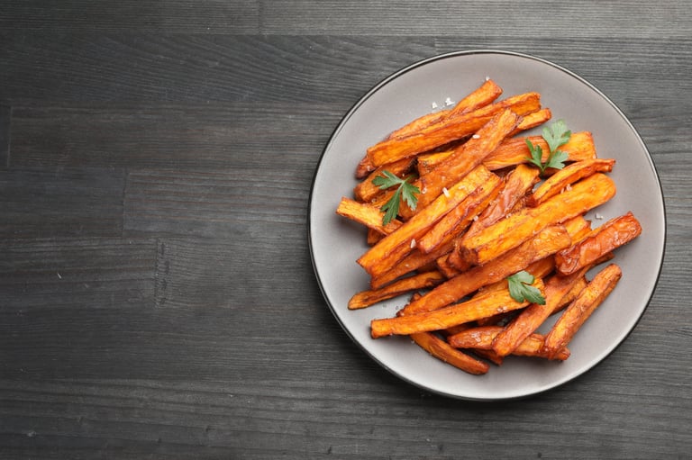 Delicious sweet potato fries with spices on black wooden table, top view. Space for text