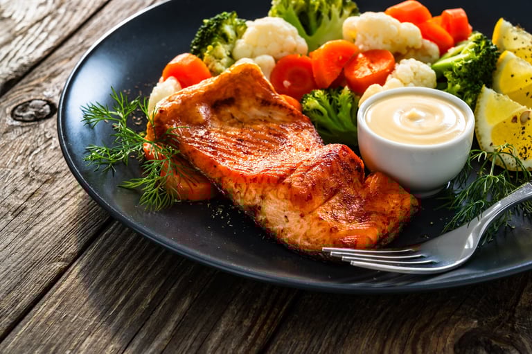Air fryer salmon steak with boiled broccoli, cauliflower, carrot and mayonnaise on wooden table
