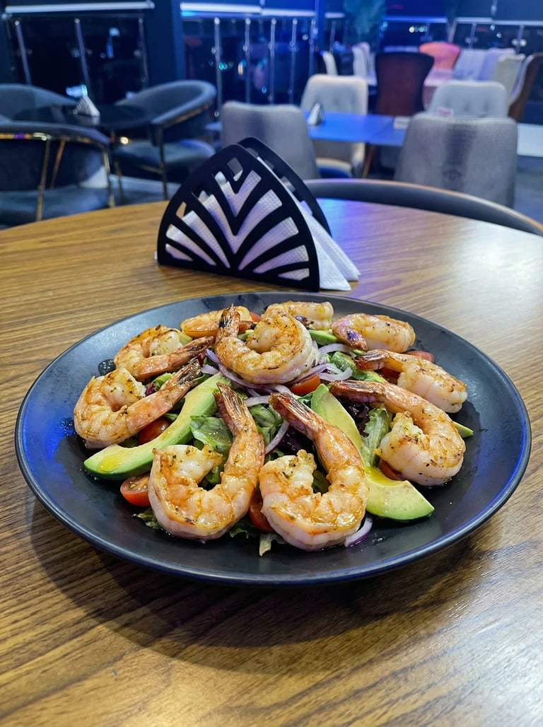 Plate of grilled shrimp with avocado and vegetables on a dark blue plate in a modern restaurant