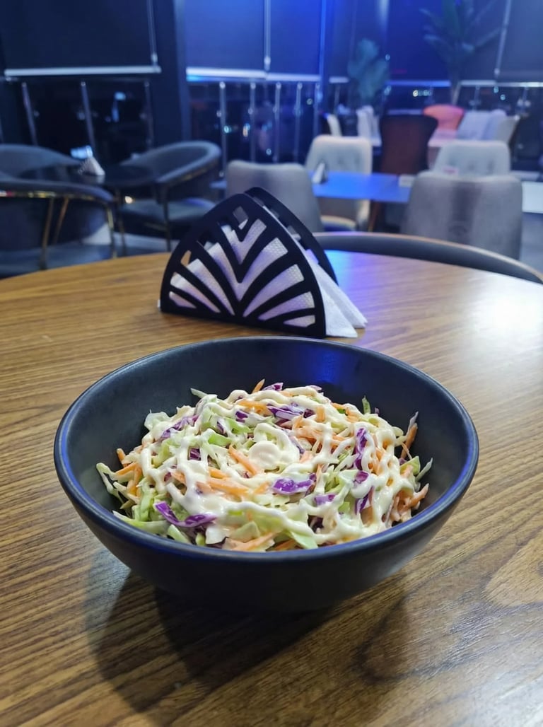 Black bowl of colorful coleslaw with striped napkin on wooden table in modern office space