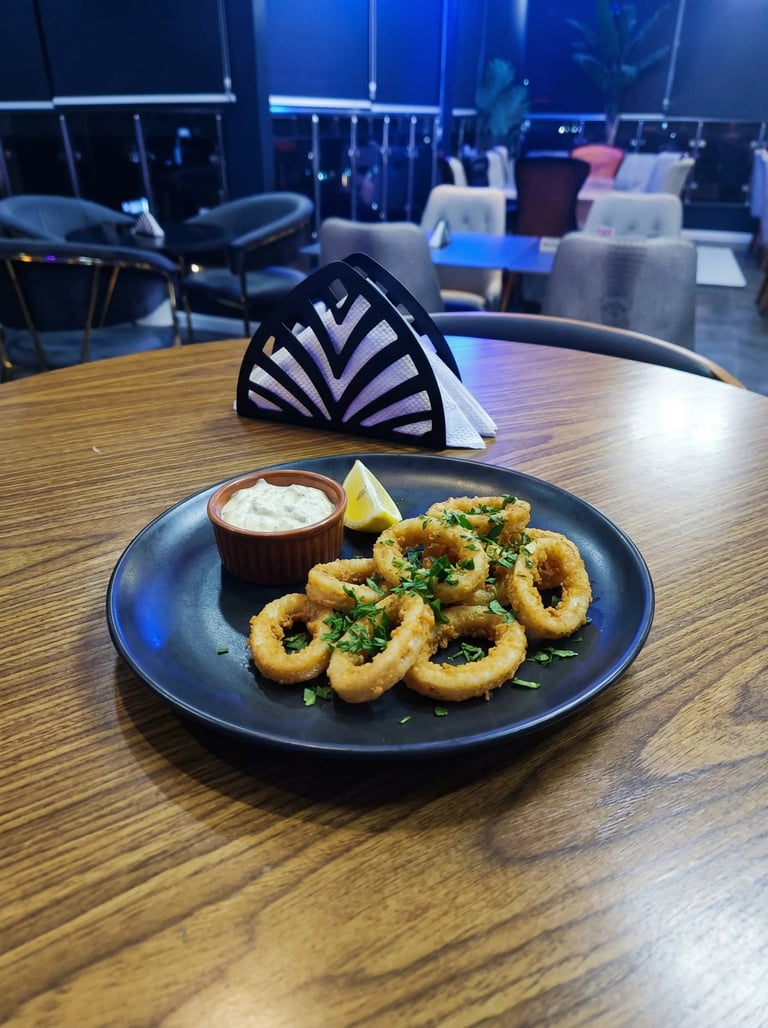 Plate of golden fried calamari with garlic, parsley, and lemon wedge on a wooden table in a modern restaurant setting